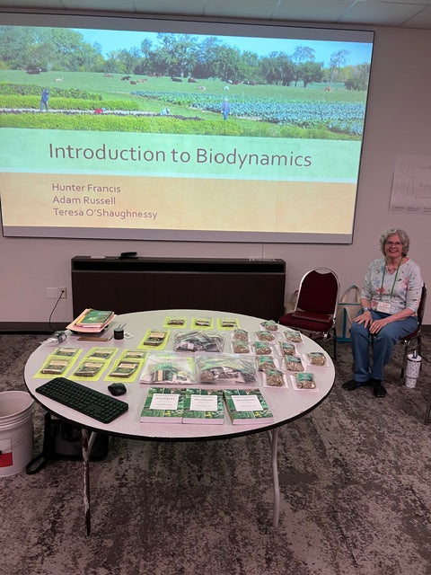 Teresa O’Shaughnessy beside a JPI display table and an Introduction to Biodynamics presentation at the Southern Family Farmers and Food Systems Conference on August 5, 2025.
