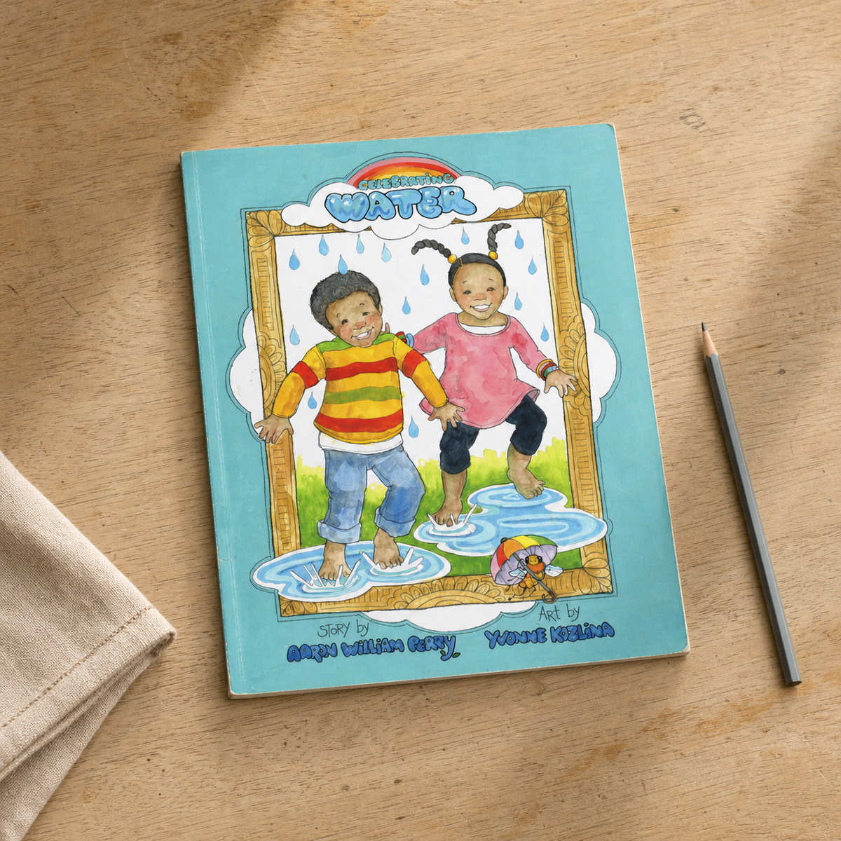 Celebrating Water by Aaron William Perry and Yvonne Kozlina — thin picture-book paperback on a natural reading desk