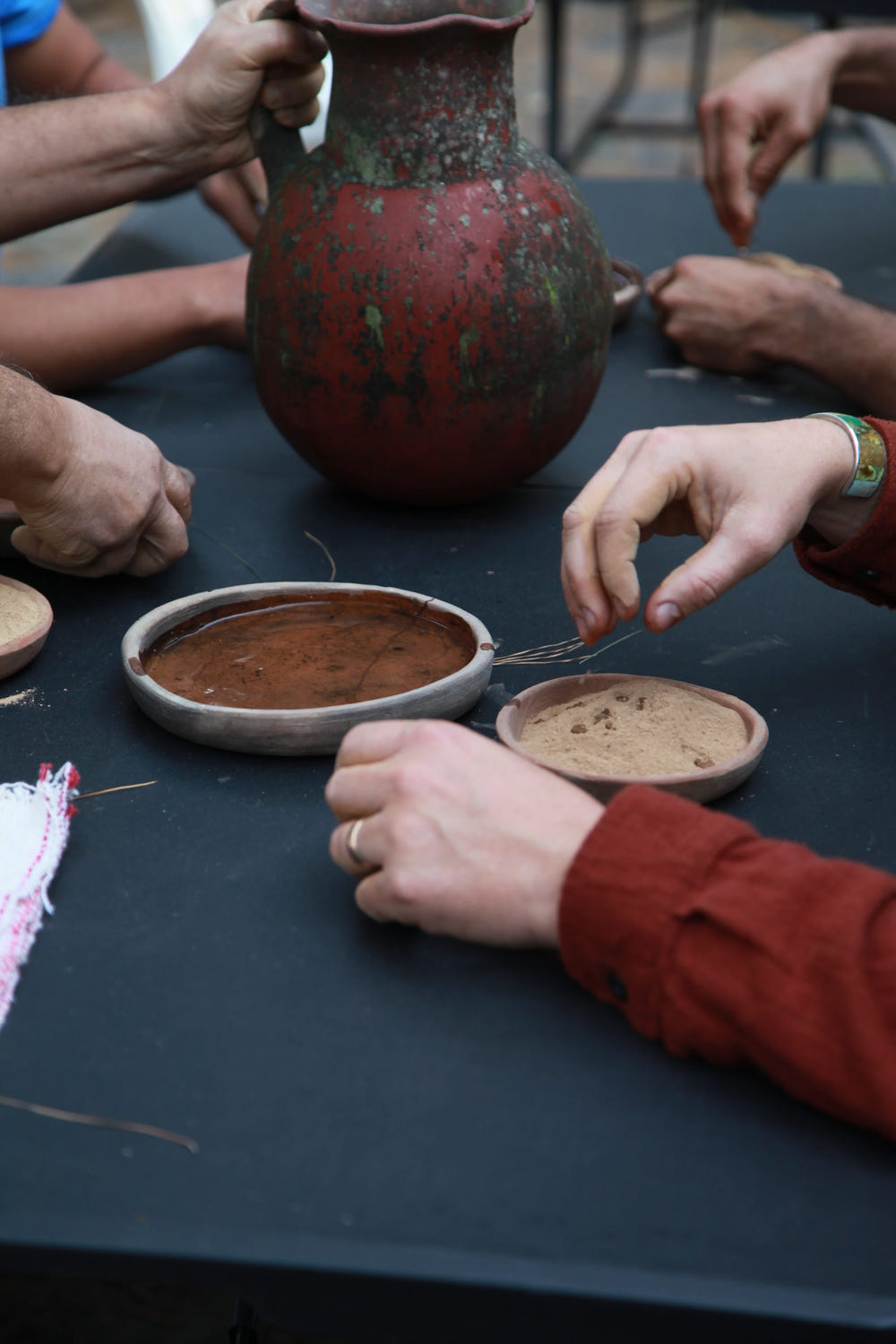 Hands gathered around earthen vessels and preparation materials