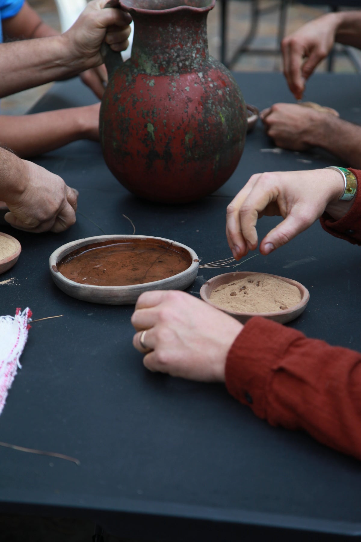 Hands gathered around earthen vessels and preparation materials
